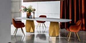 Modern dining table with geometric gold bases and red chairs in a stylish room.